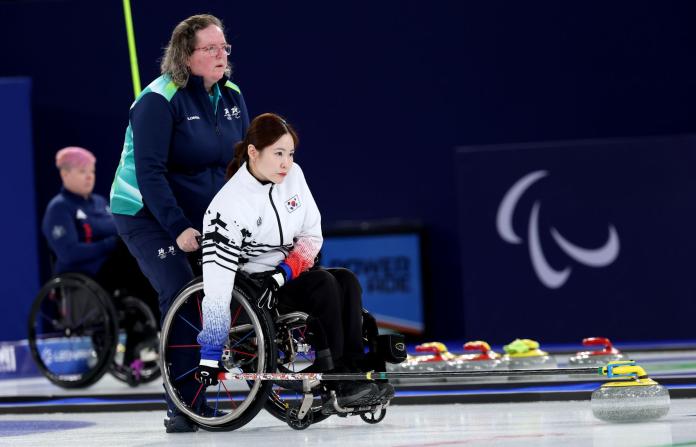 A female wheelchair curler shown as she prepares to deliver a curling stone on the ice
