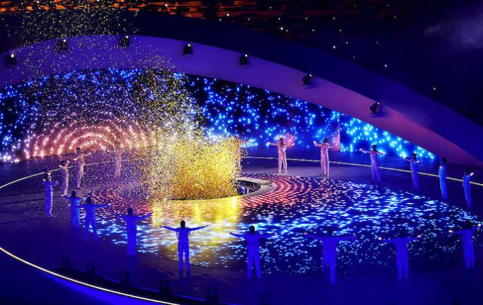 Performers in white stand in a ring around a symbolic fire