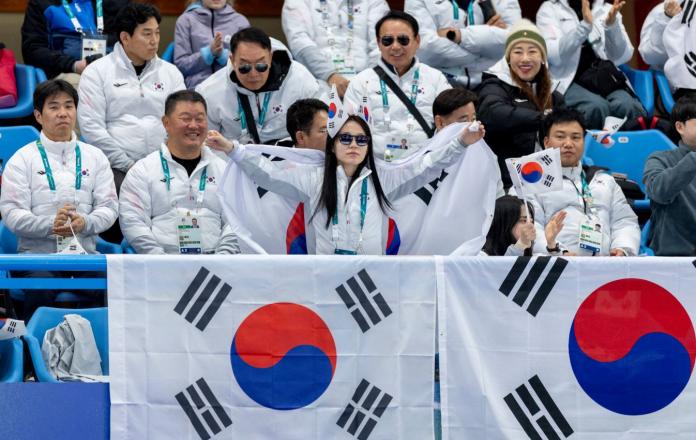 A female spectator, surrounded with other fans, waving the South Korea flag while cheering up