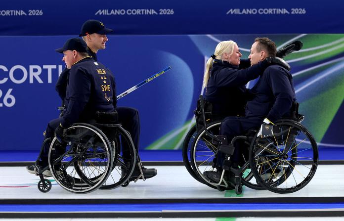 A female and male wheelchair curler embrace, while two male wheelchair curlers look on
