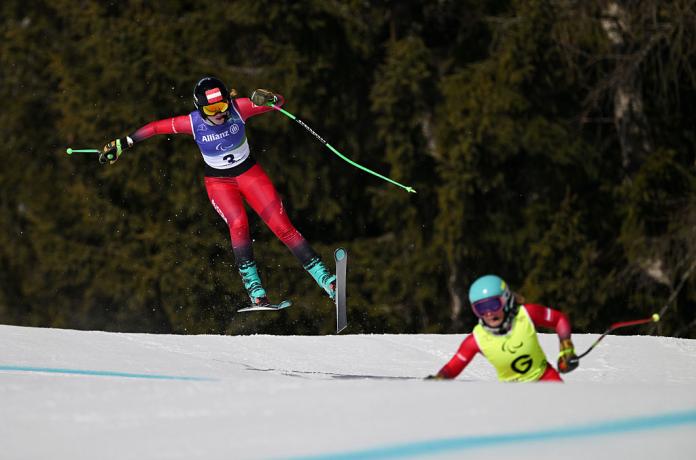 A female Para alpine skier races down, along her sighted guide