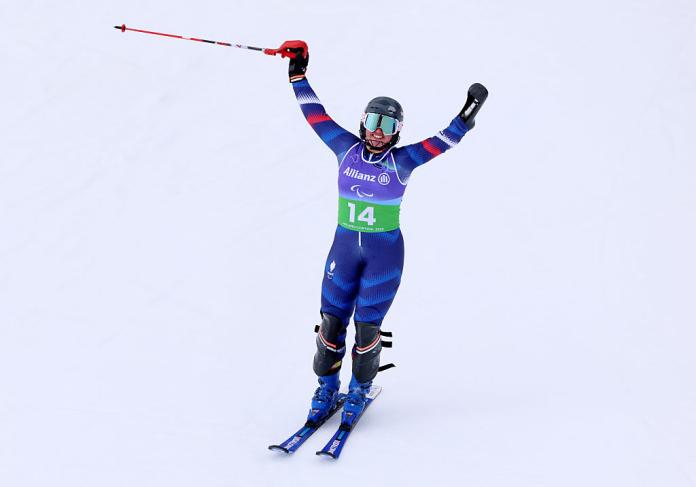 A female Para alpine skier raises both arms in celebration