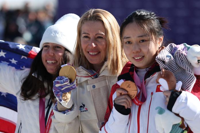 Three female Para snowboard athletes posing for a picture on the podium, holding their medals.