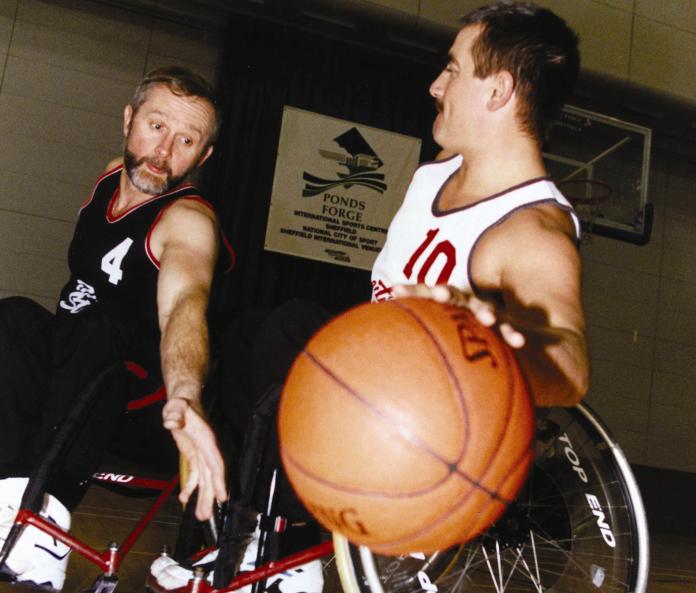 Una foto de 2 hombres en silla de ruedas jugando baloncesto.