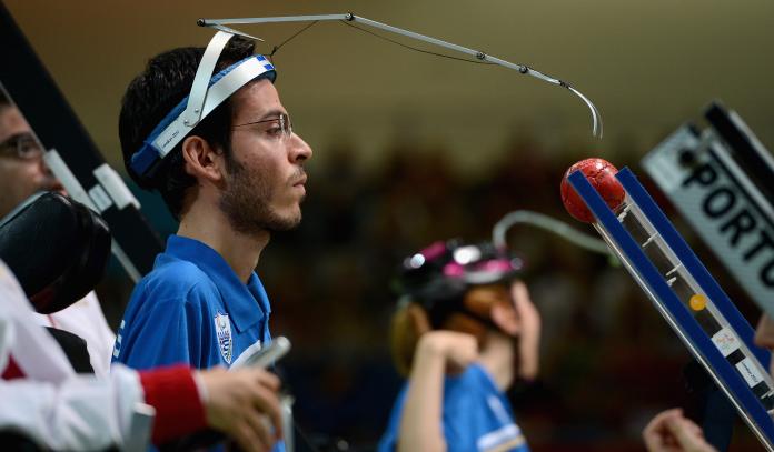 A picture of a man pushing a smal ball with a metal arm hooked to his head