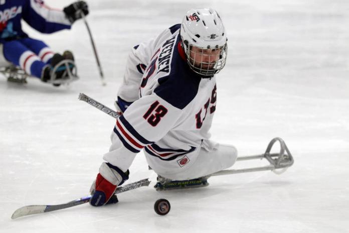 A picture of a man in a sledge playing ice hockey