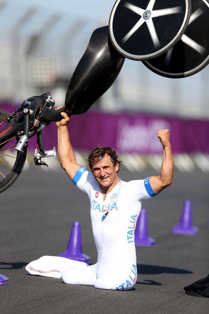 Man on a track holding a handbike above his head and smiling