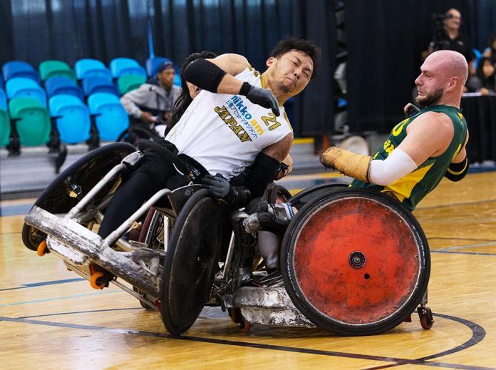 Two men playing wheelchair rugby collide their chairs. 