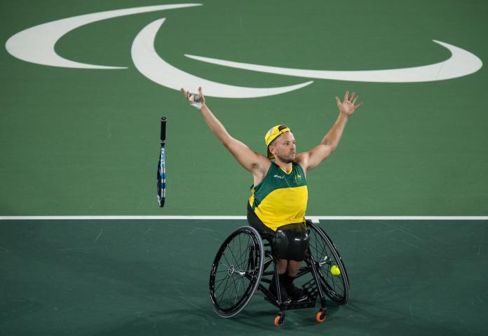 a man in a wheelchair throws his tennis racket and raises his arms to celebrate