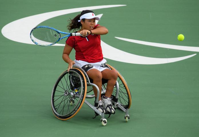 A Japanese wheelchair tennis player is hitting the ball.