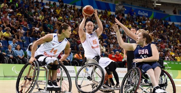 A woman in a wheelchair shoots a basketball while being challenged by two other wheelchair athletes