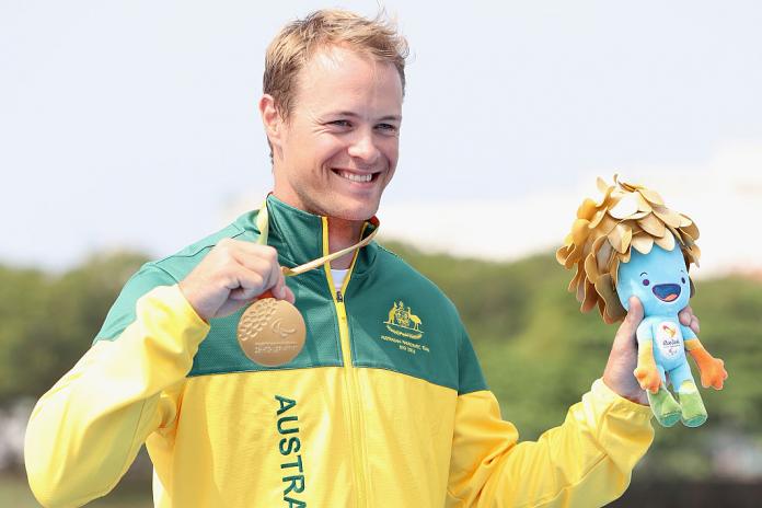 a man holds up his gold medal on the podium