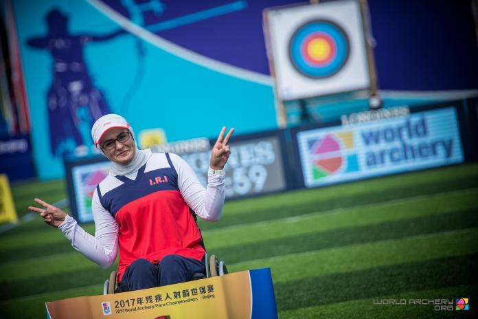 Female archer poses in front of a target