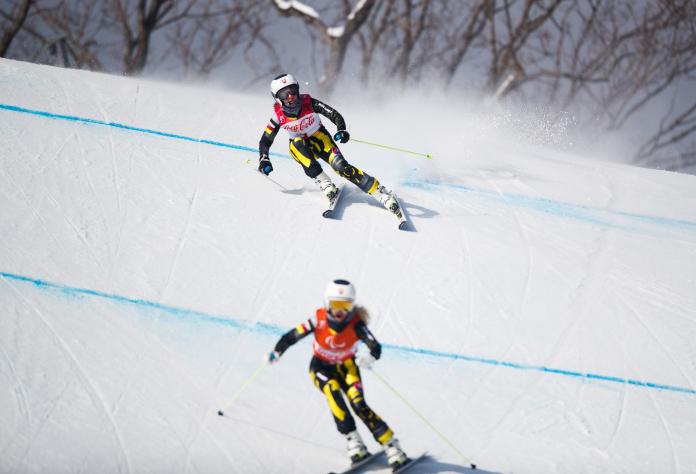 a female vision impaired skier and her guide head down the slope