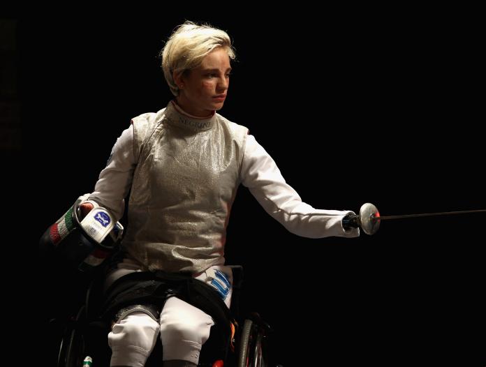 a female wheelchair fencer holds up her foil