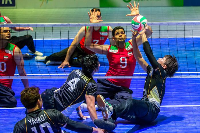 Japanese sitting volleyball player sets the ball while an Iranian athlete prepares to block