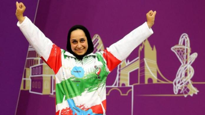 female Para shooter Sareh Javanmardi raises her arms on the podium