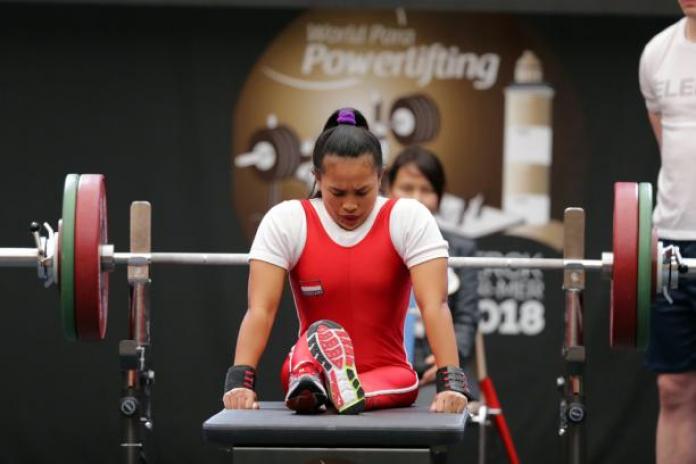Woman bows head as she sits on powerlifting bench preparing to lift the bar