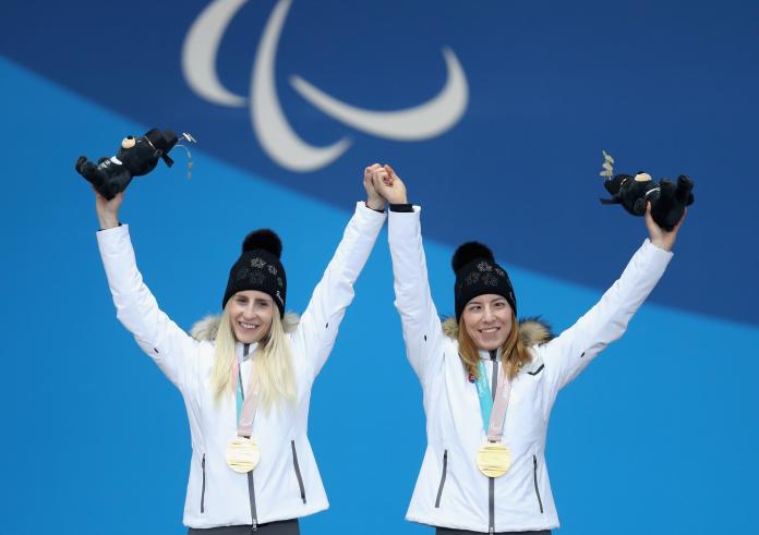 female Para skier Henrieta Farkasova and her female guide holding their arms up on the podium with gold medals around their necks