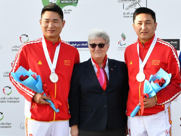 Chinese Para shooters Yang Chao and Huang Xing standing either side of a woman and smiling on the podium