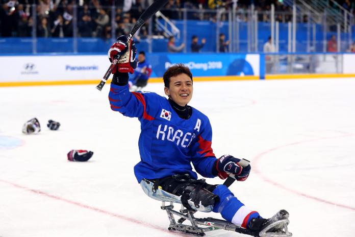 male Para ice hockey player Seung-Hwan Jung waves his stick in celebration on the ice