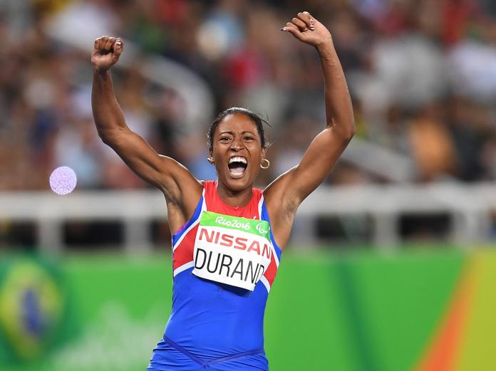 female vision impaired sprinter Omara Durand raises her arms and cheers as she crosses the finish line to win