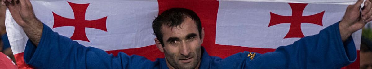 a male judoka holds up the Georgia flag