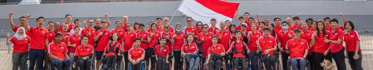 A group photo taken in front of a national stadium in Singapore. About 50 people are wearing red T-shirts.