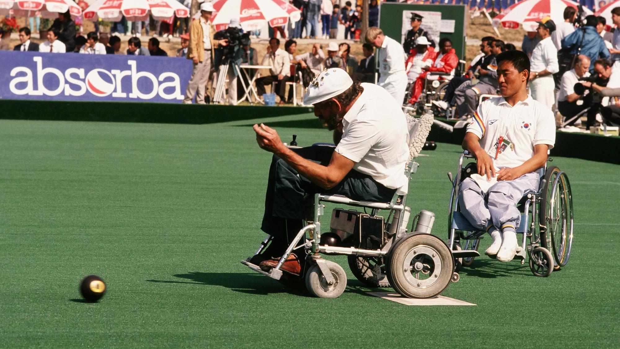 Boccia player on a wheelchair throws the jack while another one observes