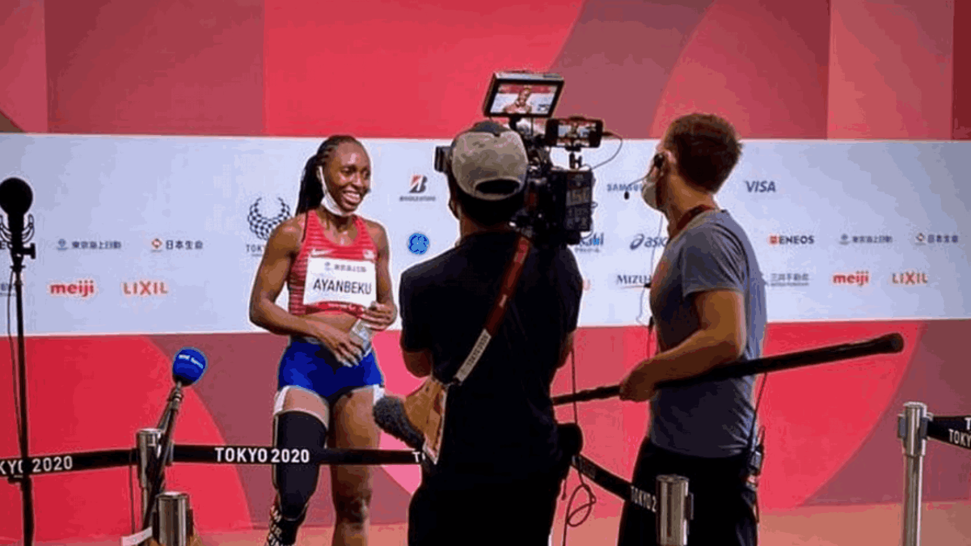 A female sprinter talks to two men carrying filming equipment at the Tokyo 2020 Paralympic Games.