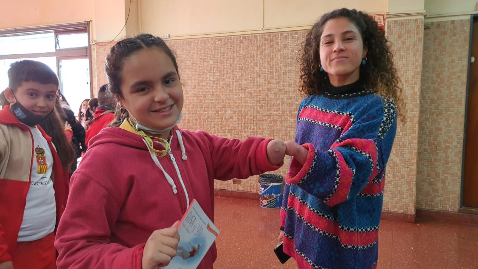 A young girl and a Para athlete, both missing their left hands, bump their arms together at a school.