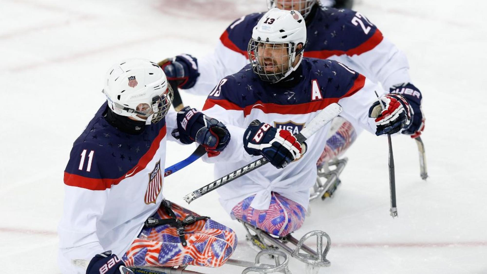 An ice sledge hockey player skates up to his teammate to celebrate.