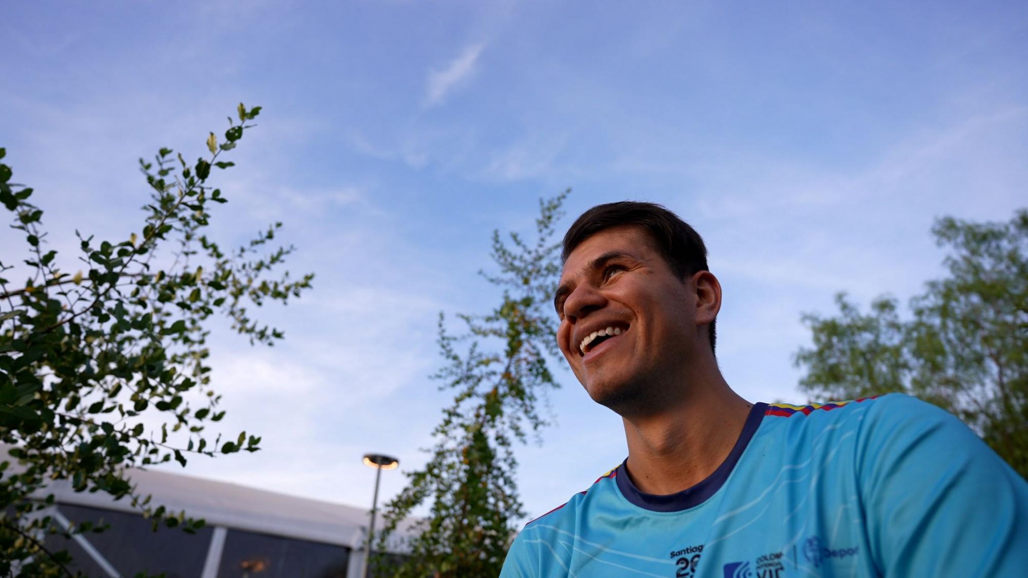 Jhon Gonzalez, a blind football player from Colombia, is standing outdoors wearing a blue uniform