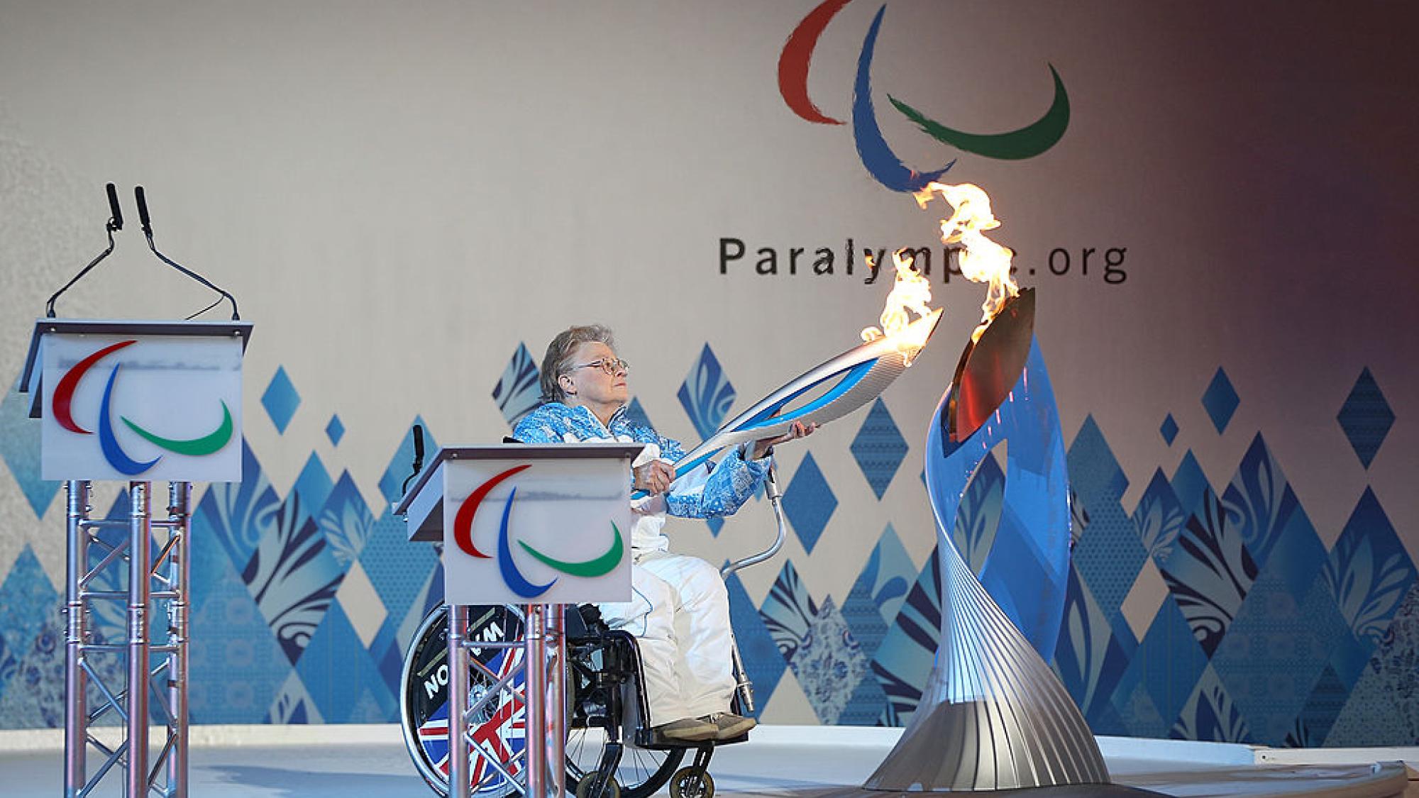 Paralympian Caz Walton is holding a torch in front of a silver cauldron