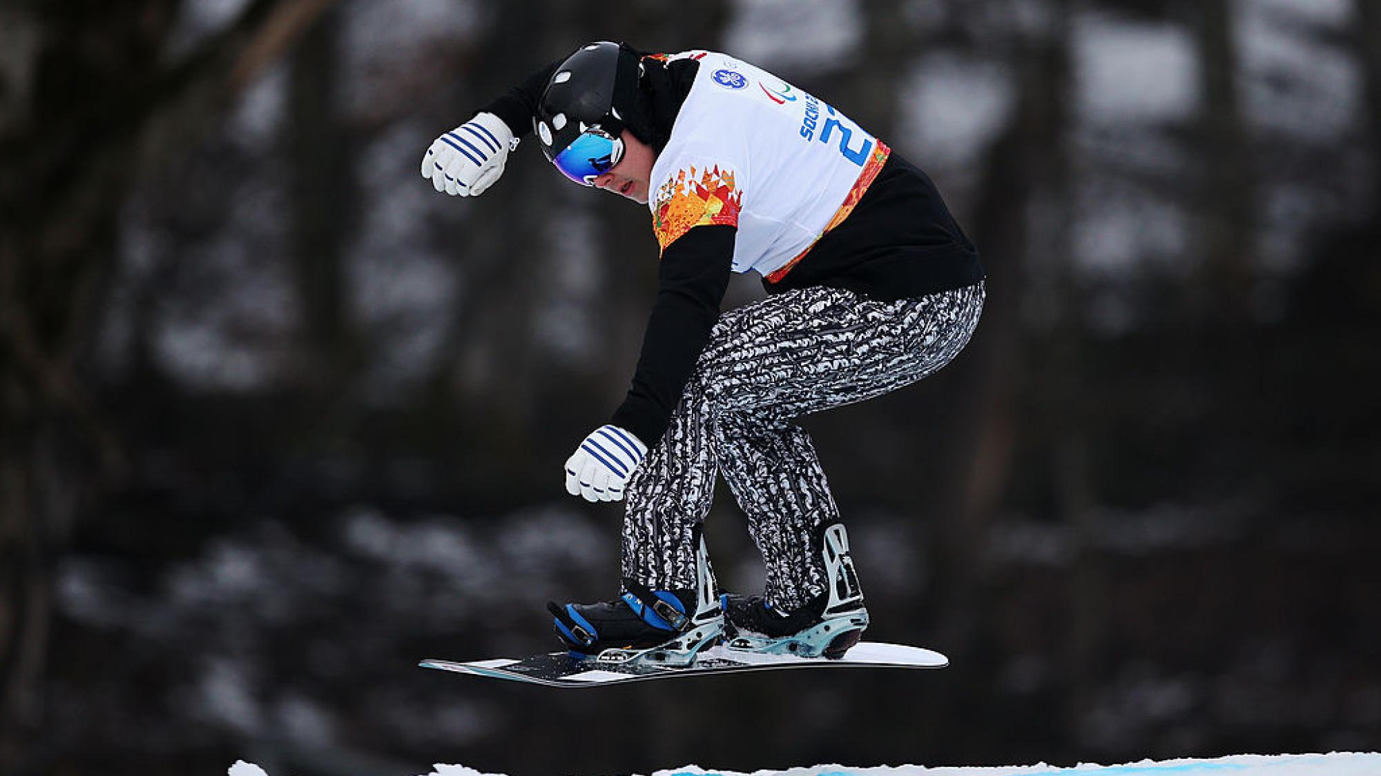 A male Para snowboarder makes a jump during a competition