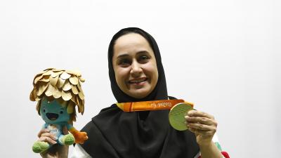 Woman with headscarf poses with medal and mascot in her hand