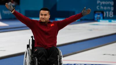 a male wheelchair curler raises his arms in celebration