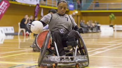 Woman in wheelchair rugby chair secures the ball with right hand