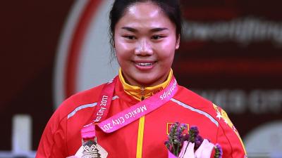 female powerlifter Yujiao Tan holds up her gold medal and a bunch of flowers