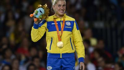 female judoka Inna Cherniak holds up a mascot teddy and her medal on the podium