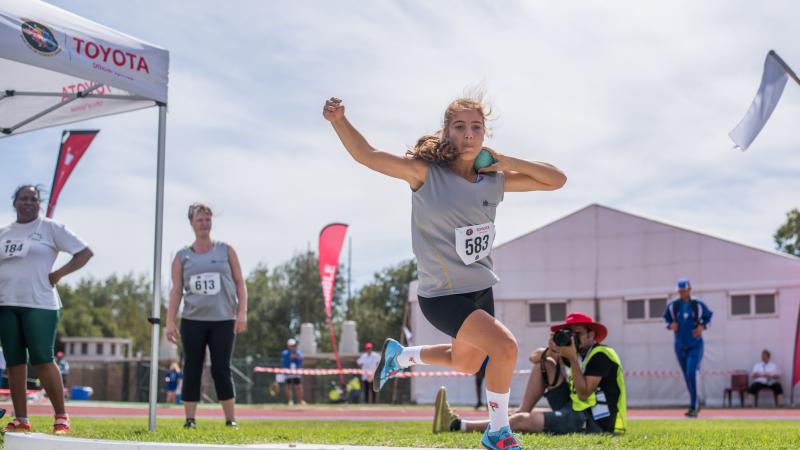 A female teenage athlete competing in shot put watched by three people