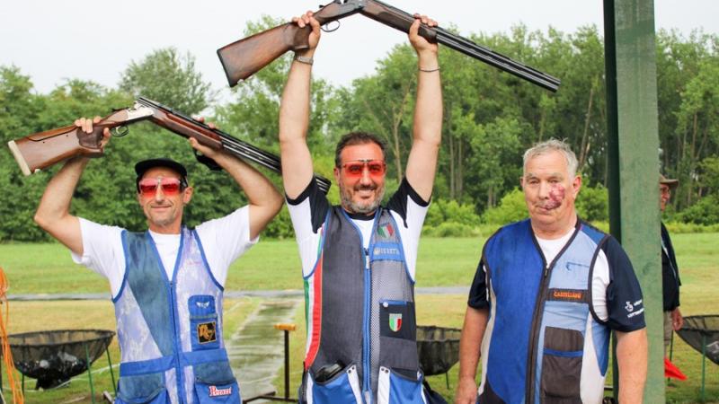 Three male Para trap shooters pose together with man in middle raising his shot gun over his head