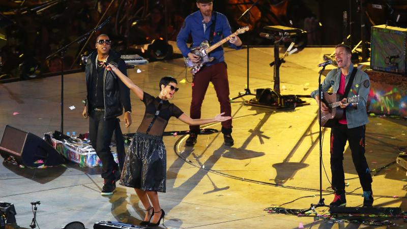 three singers, Jay Z, Rihanna and Chris Martin from Coldplay singing on a stage and waving