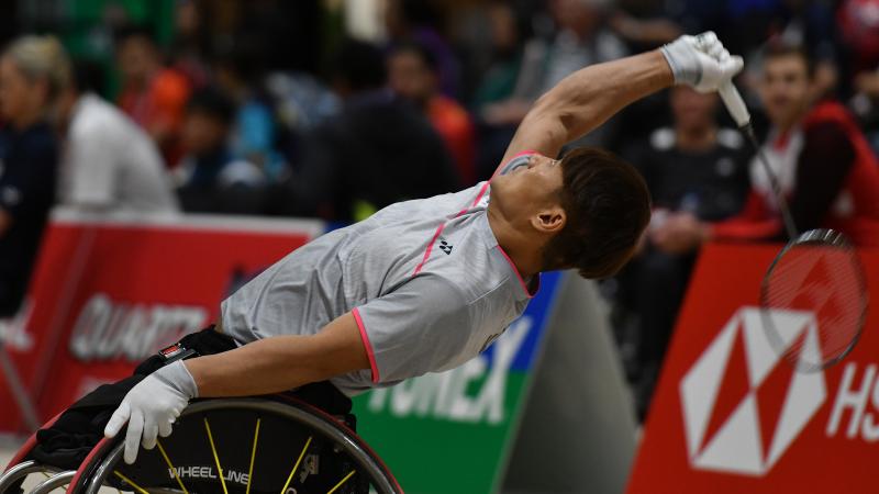 a male wheelchair badminton player leans back to hit a shot