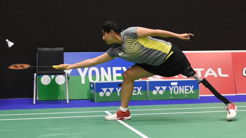 a female Para badminton player with a prosthetic leg reaches for a shot