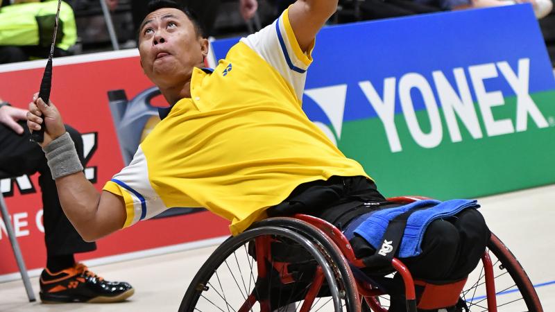 a male wheelchair badminton player leans back to hit a shot