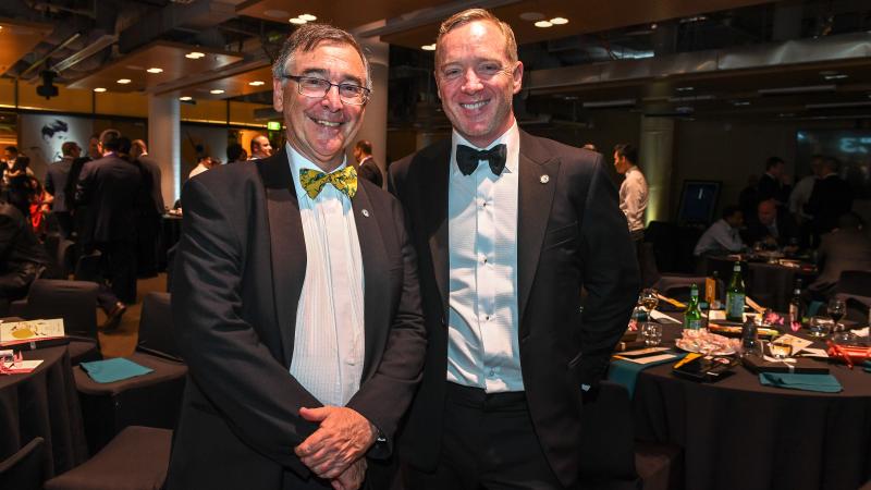 two men in suits standing and smiling at the camera