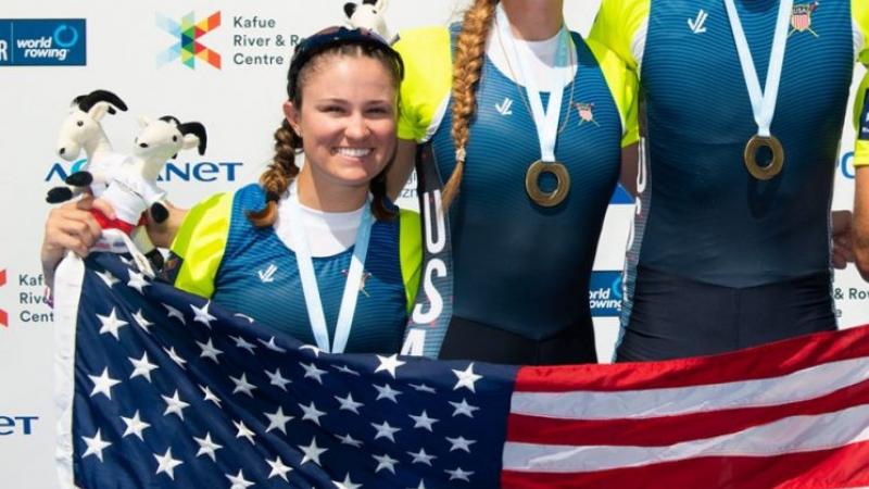 Female rower smiles on podium holding USA flag