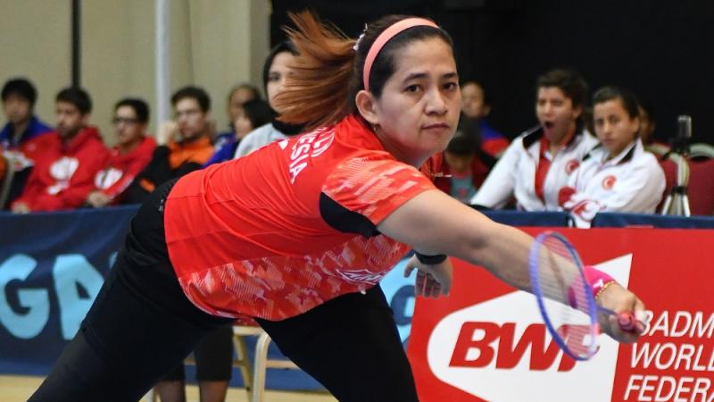 A female Para badminton player leans down to hit a forehand