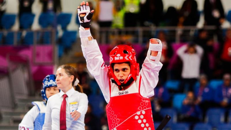 a female Para taekwondo athlete raises her arms in celebration